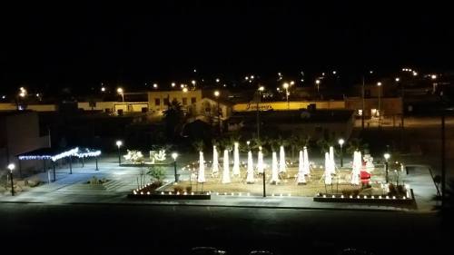 A nighttime view of a plaza with illuminated umbrellas, lights, and surrounding buildings in a quiet setting.
