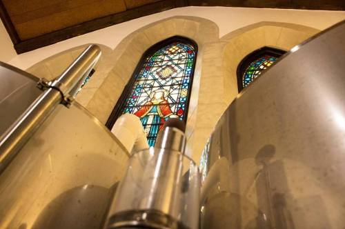 Close-up of shiny metal tanks with a stained glass window in the background, featuring colorful designs and arches.