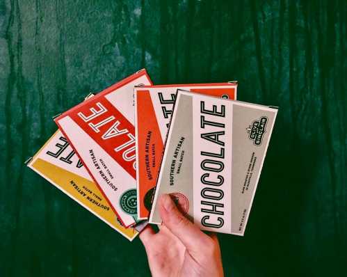 A hand holding several colorful chocolate bars against a green background.