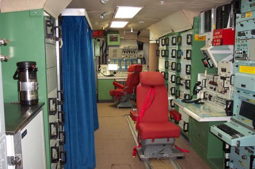Interior of a control room with green walls, red chairs, and various control panels and equipment.