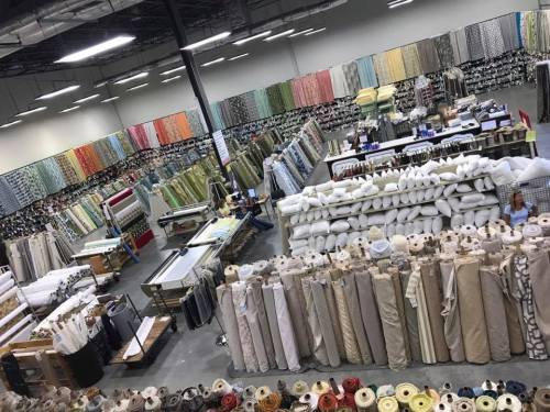 A spacious fabric store filled with colorful rolls of fabric and neatly stacked pillows, organized in rows.