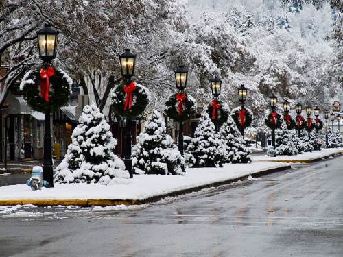 Snow-covered street lined with festive lampposts and decorated evergreen trees, creating a winter wonderland scene.