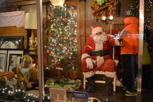 A festive window display featuring Santa Claus, a Christmas tree, and a child in winter clothing.