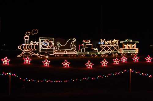 A brightly lit train with a sleigh and gifts, decorated with colorful lights and stars, set against a dark night sky.