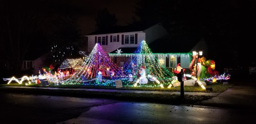 A house decorated with colorful Christmas lights, featuring snowmen, Santa, and festive displays in the yard.