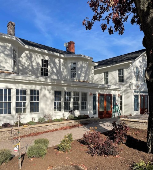 A modern two-story house with white siding, large windows, and a landscaped yard under a clear blue sky.