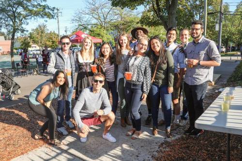 A group of diverse friends poses together outdoors, smiling and holding drinks at a sunny gathering.
