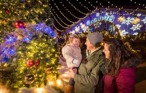A joyful family stands by a decorated Christmas tree, surrounded by festive lights and decorations.