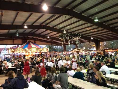 A lively indoor festival scene with people dining, a carousel, and festive decorations in a large gathering space.