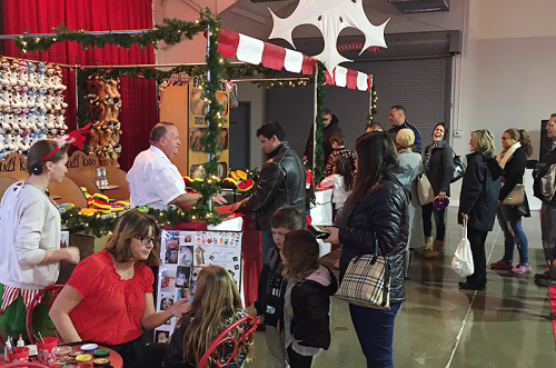 A festive market scene with people shopping, a vendor at a decorated stall, and holiday decorations in the background.