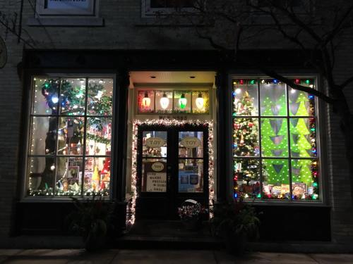 A festive toy store window decorated with colorful lights, a Christmas tree, and holiday decorations.