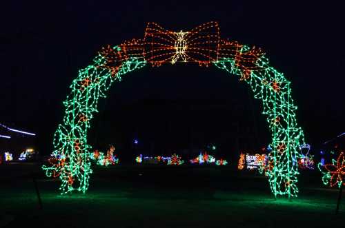 A colorful arch made of Christmas lights, adorned with a large bow, set against a dark night sky.