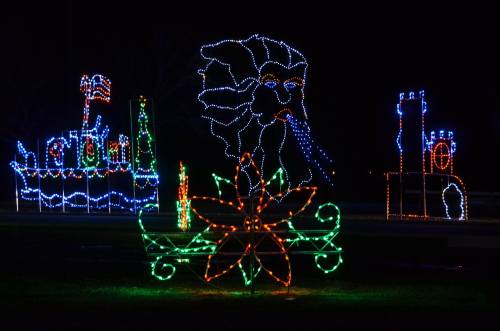 Colorful holiday lights display featuring a ship, castle, and a large flower in a nighttime setting.