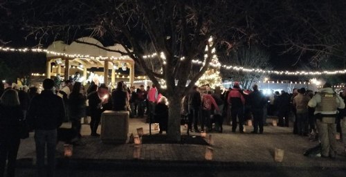 A crowd gathers at night under string lights, with a festive atmosphere and a decorated tree in the background.