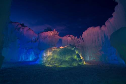 Colorful ice formations illuminated in blue, purple, and pink light, creating a magical winter landscape at night.