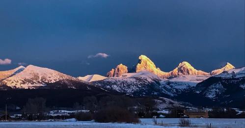 Sunlit snow-capped mountains under a dramatic sky, showcasing peaks with golden highlights at sunset.
