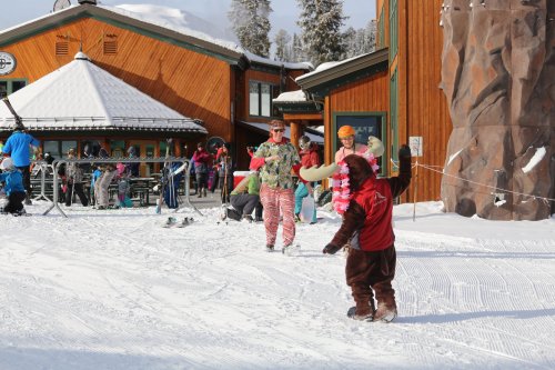 A snowy ski resort scene with people in colorful outfits, including someone in a moose costume, enjoying the winter day.