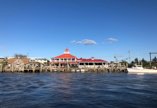 A waterfront scene featuring a restaurant with a red roof, wooden docks, and a clear blue sky.