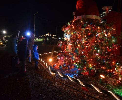 A child gazes at a brightly lit Christmas tree surrounded by festive decorations at night.