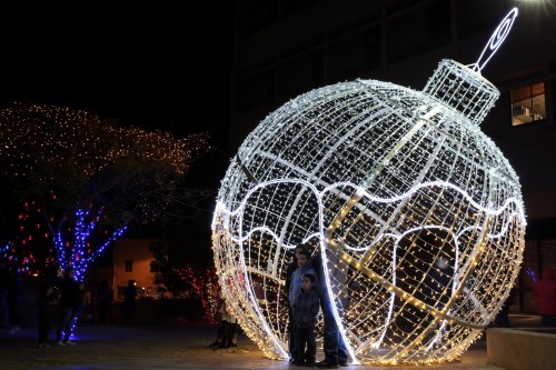 A large illuminated Christmas ornament with people standing inside, surrounded by festive lights at night.