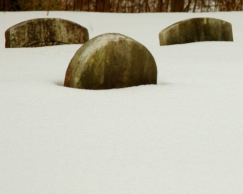 Three rounded gravestones partially covered in snow, surrounded by a serene winter landscape.