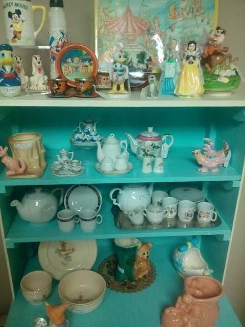 A colorful display of vintage collectibles, including teapots, figurines, and various ceramic items on a teal shelf.