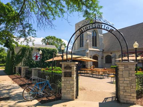 A stone archway leads to a Biergarten with outdoor seating, surrounded by greenery and a blue bicycle parked nearby.