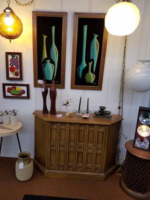 A vintage display featuring a wooden cabinet, decorative vases, artwork, and various decorative items in a cozy setting.