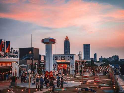 A vibrant amusement park scene at sunset, featuring rides, games, and city skyline in the background.