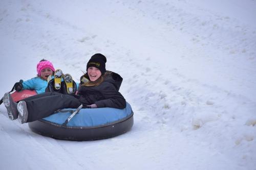 Two children joyfully tubing down a snowy slope, wearing winter gear and smiling in the cold weather.