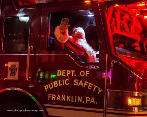 Santa Claus waves from a fire truck, decorated with lights, during a festive event in Franklin, PA.