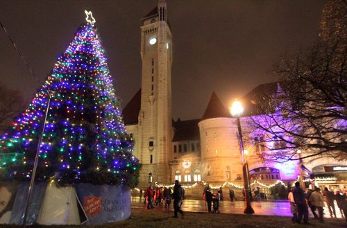 A brightly lit Christmas tree in front of a historic building at night, with festive lights and people gathered around.