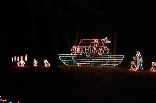 Colorful holiday lights depict a boat with figures and animals in a dark forest setting.