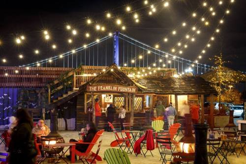 A cozy outdoor scene at night with string lights, a wooden stand, and people enjoying the atmosphere near a bridge.