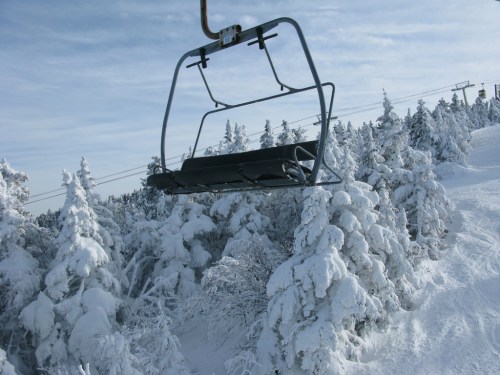 A ski lift chair suspended above snow-covered trees in a winter landscape.