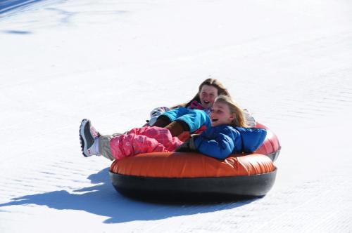 Two girls joyfully tubing down a snowy slope, wearing colorful winter gear and laughing together.
