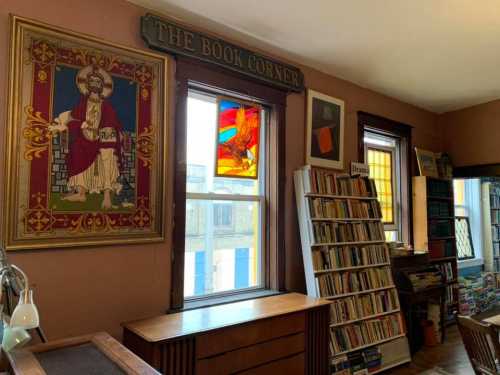 Cozy book corner with stained glass windows, a large painting, and shelves filled with books. Warm, inviting atmosphere.