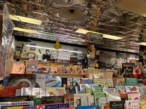 A cozy bookstore filled with colorful children's books and a shiny, reflective ceiling.