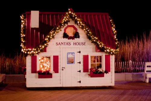 A festive small house decorated with lights and wreaths, labeled "Santa's House," set against a dark night sky.
