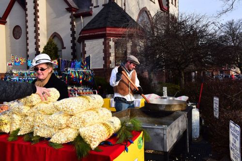 A vendor sells popcorn at an outdoor market, while another cooks nearby, with a church in the background.