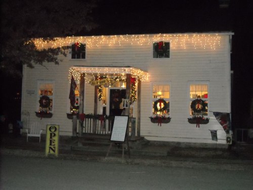 A charming white building decorated with Christmas lights and wreaths, illuminated at night, with an "Open" sign outside.