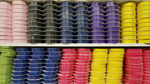 A shelf filled with neatly arranged rolls of colorful tape in various shades, including pink, black, blue, purple, and yellow.