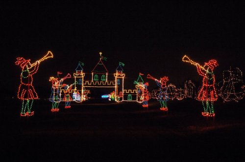 Colorful holiday lights depict a castle with trumpet-playing figures in a festive nighttime scene.
