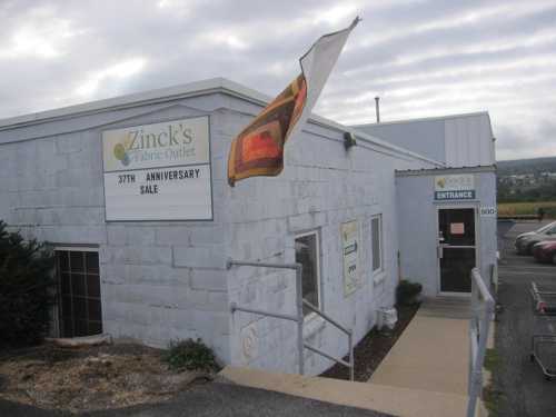 Exterior of Zinck's Fabric Outlet with a sign for a 37th anniversary sale and an entrance door.