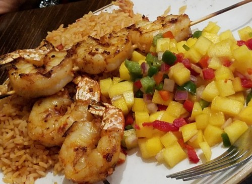 Grilled shrimp skewers served with rice and a colorful mango and vegetable salsa on a white plate.
