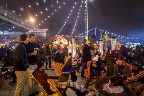 A lively outdoor market at night, with string lights, people socializing, and festive decorations.