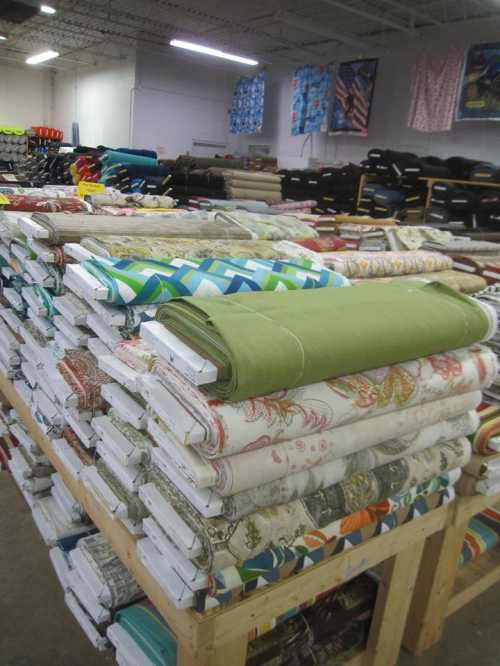 A large display of neatly stacked fabric rolls in a bright, spacious store. Various colors and patterns are visible.