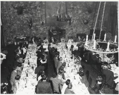A large dining room filled with people seated at a long table, surrounded by stone walls and rustic decor.