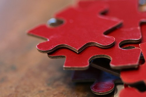 Close-up of interlocking red puzzle pieces stacked on a wooden surface.
