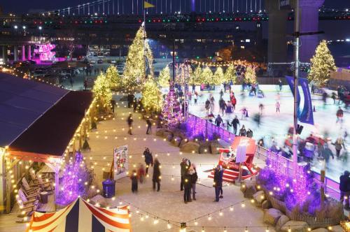 A festive outdoor ice skating rink surrounded by twinkling lights and decorated trees at night.